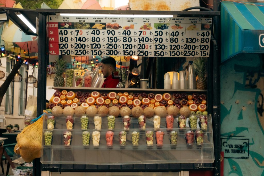 Vibrant street juice stand displaying fresh fruits and prices in a lively outdoor market.