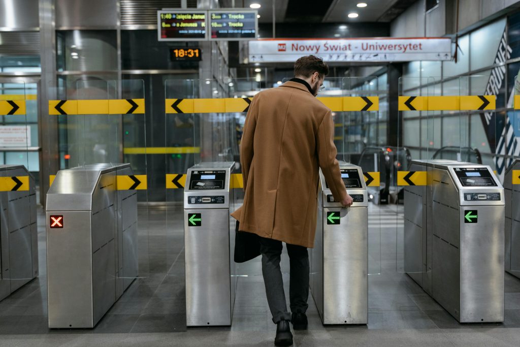Man in a brown coat using a ticket barrier at an urban train station.