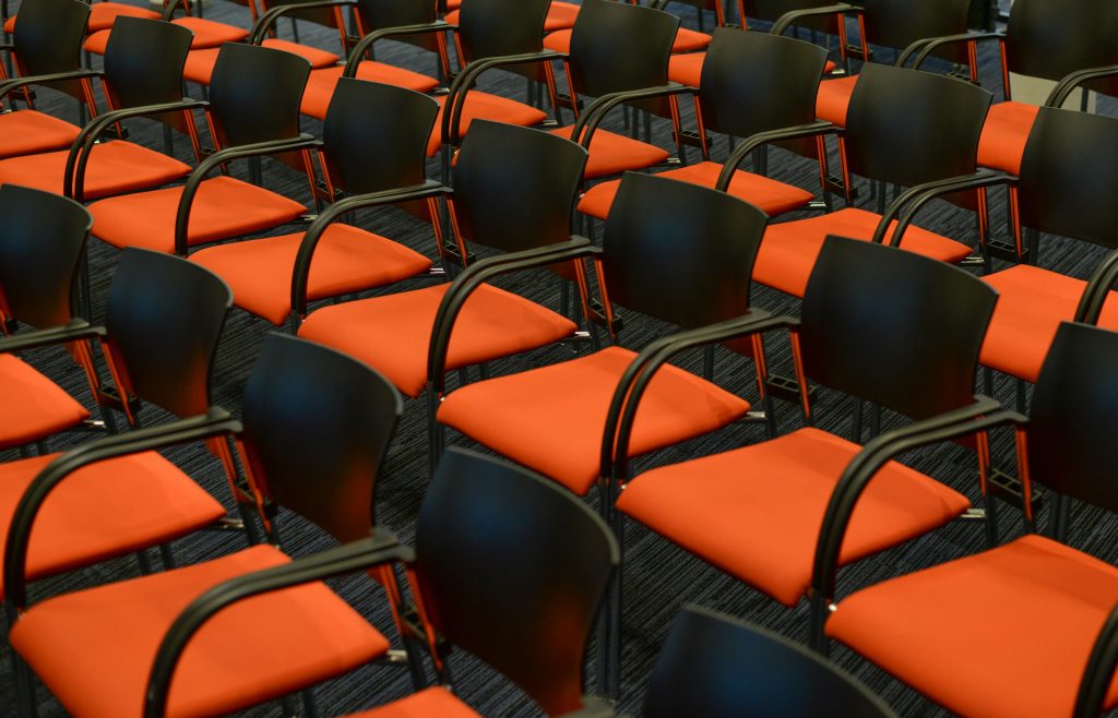 A modern auditorium with rows of empty black and orange chairs, ready for an event.