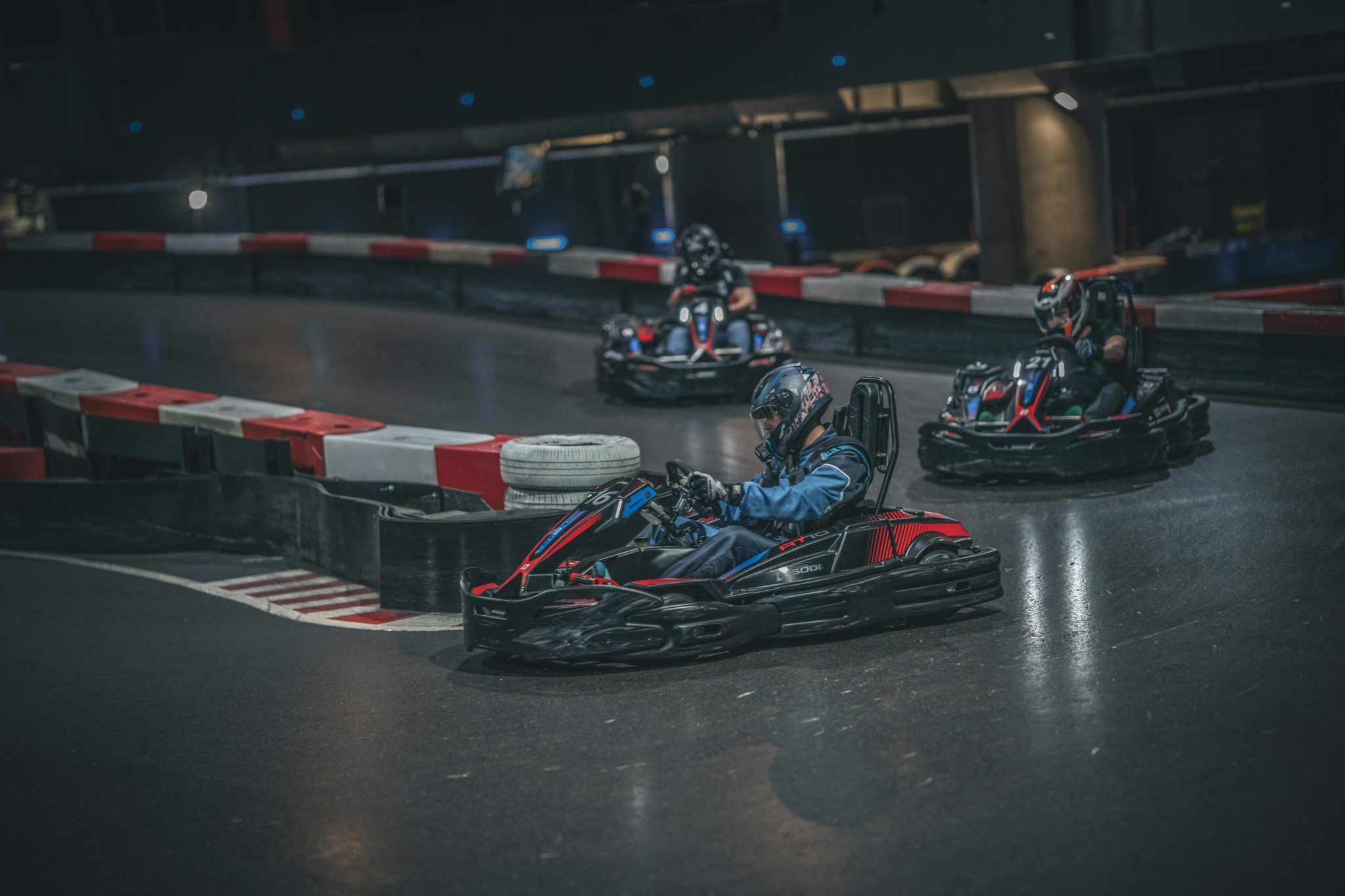 Thrilling indoor go-kart race with adult drivers taking sharp turns on track.